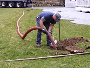 Septic pumping technician servicing a residential septic tank with a vacuum hose in Tulsa, OK