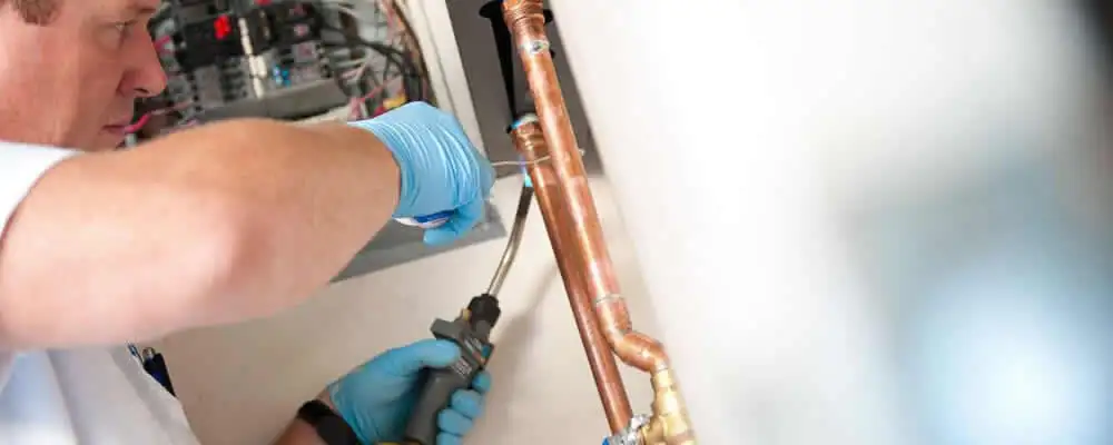 Water heater repair technician testing copper pipe connections and controls in Tulsa, OK